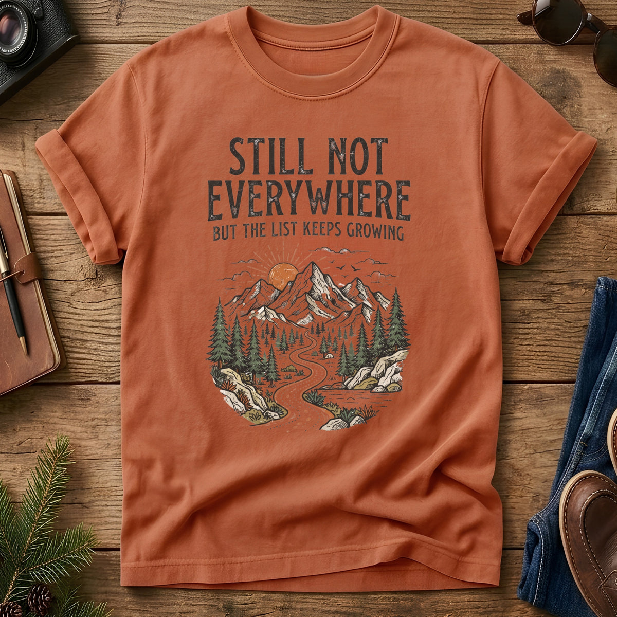 Still Not Everywhere Tee – mountain river valley sunrise graphic on Comfort Colors 1717 tee, flat lay