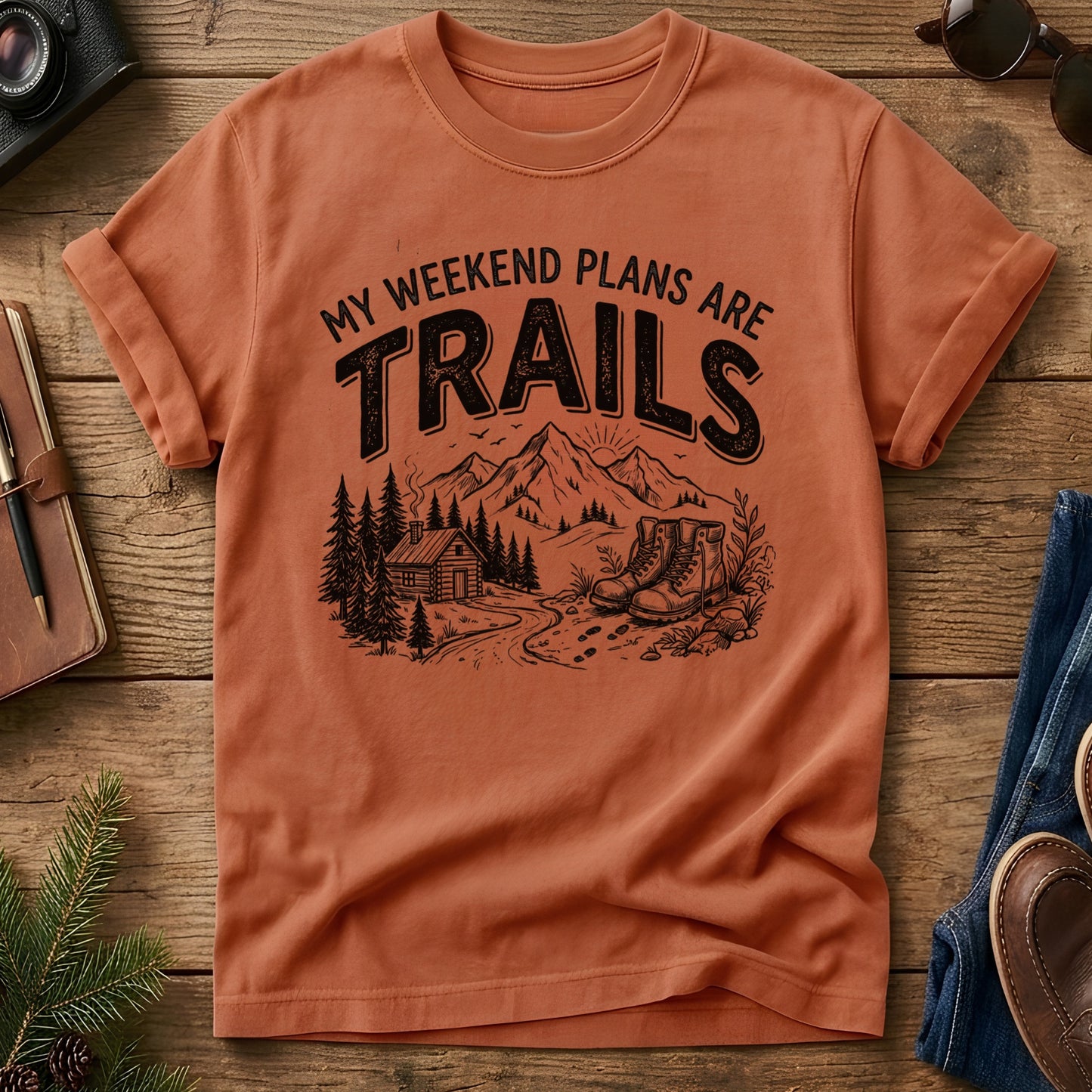 My Weekend Plans Are Trails Tee in Yam — cabin, mountain, and hiking boots graphic