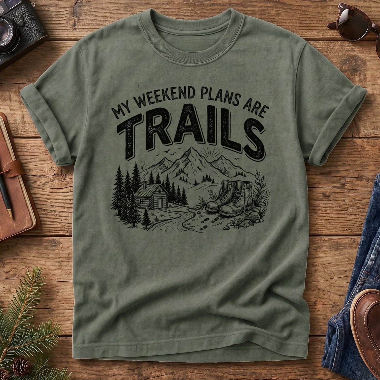 My Weekend Plans Are Trails Tee in Moss — cabin, mountain, and hiking boots graphic