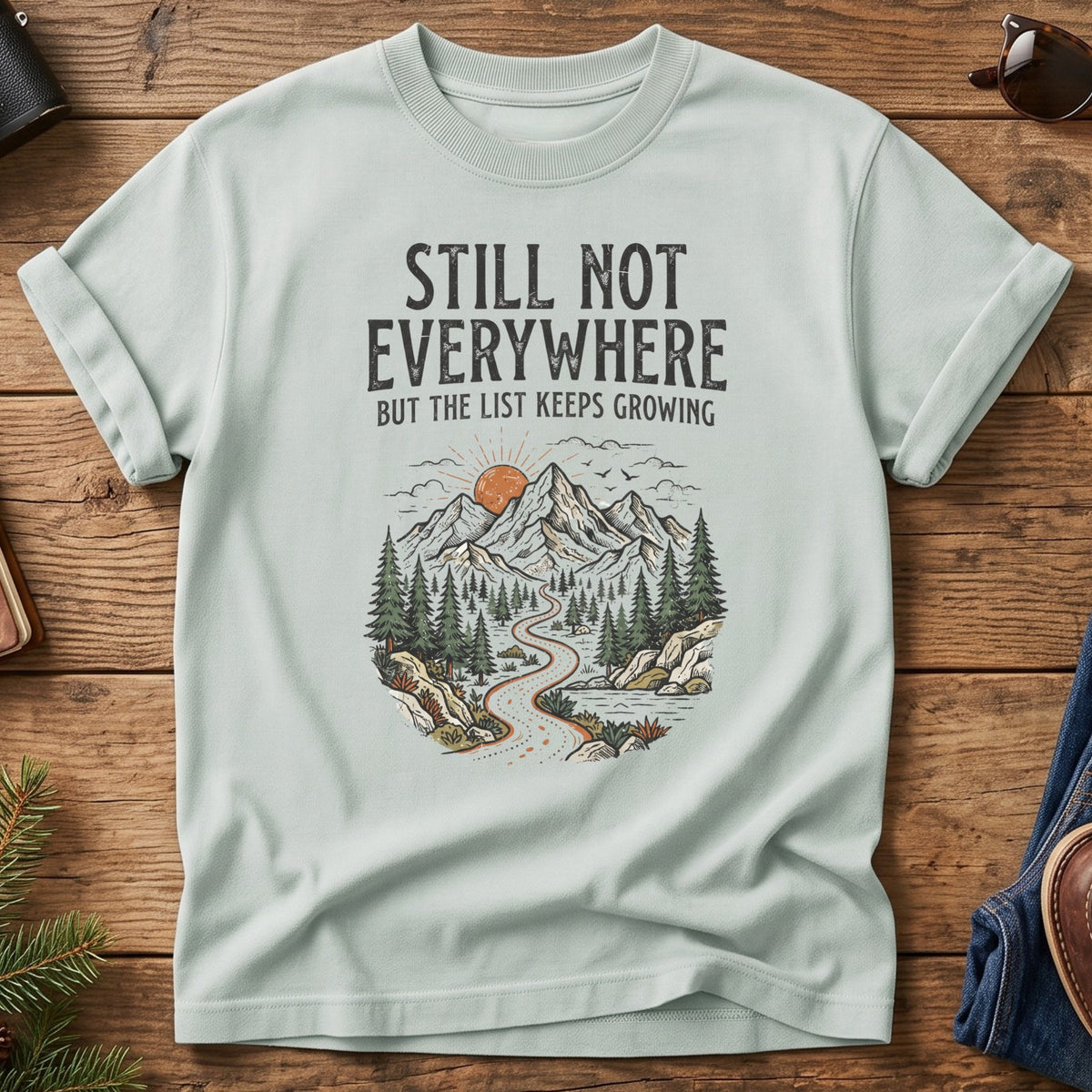 Still Not Everywhere Tee – mountain river valley sunrise graphic on Comfort Colors 1717 tee, flat lay