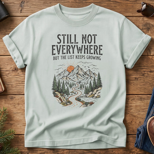 Still Not Everywhere Tee – mountain river valley sunrise graphic on Comfort Colors 1717 tee, flat lay